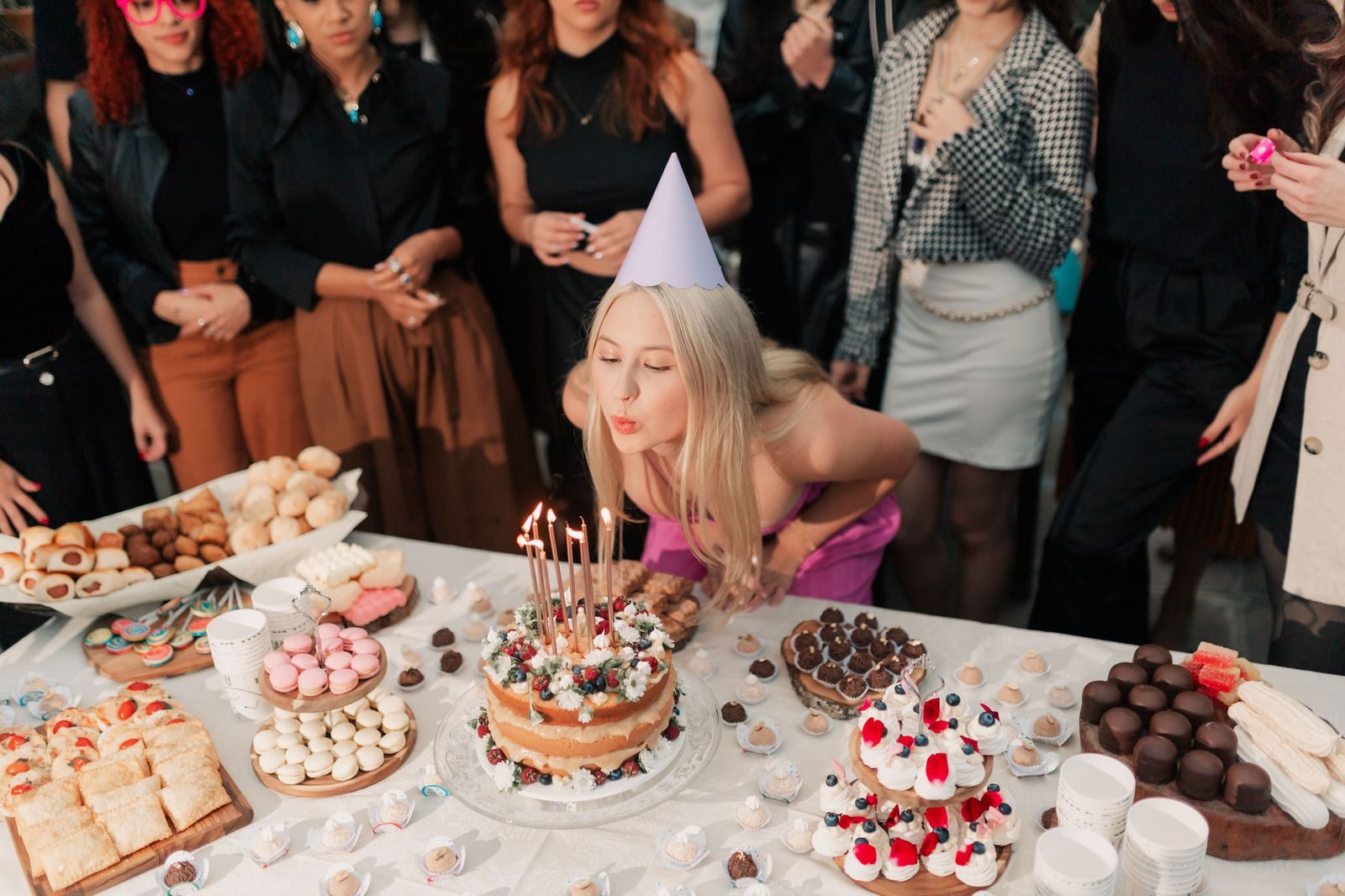 A birthday cake with candles on a dinner table surrounded by friends