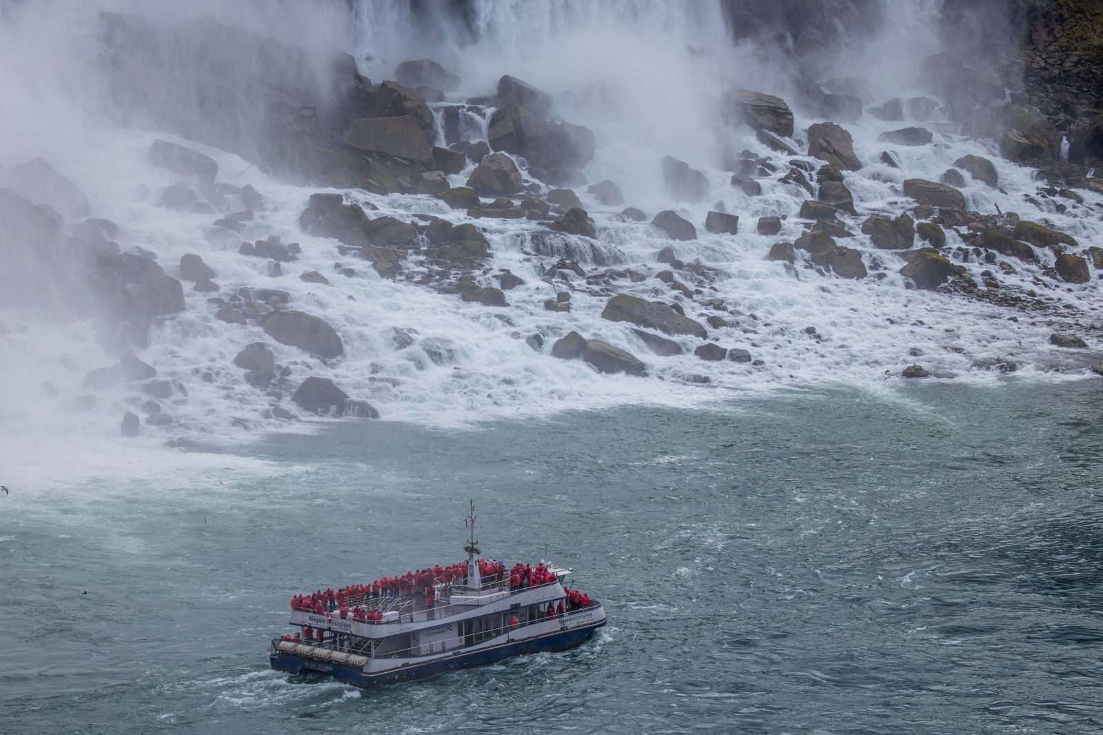 Tourists in red ponchos on a boat tour below the falls