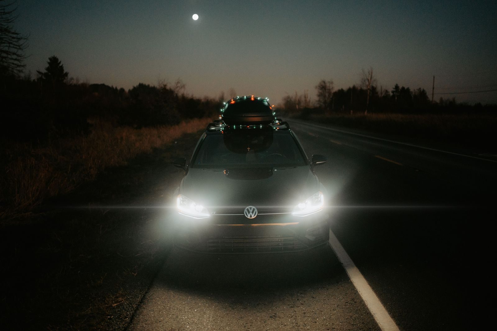 A black SUV on a dark highway with headlights on at night