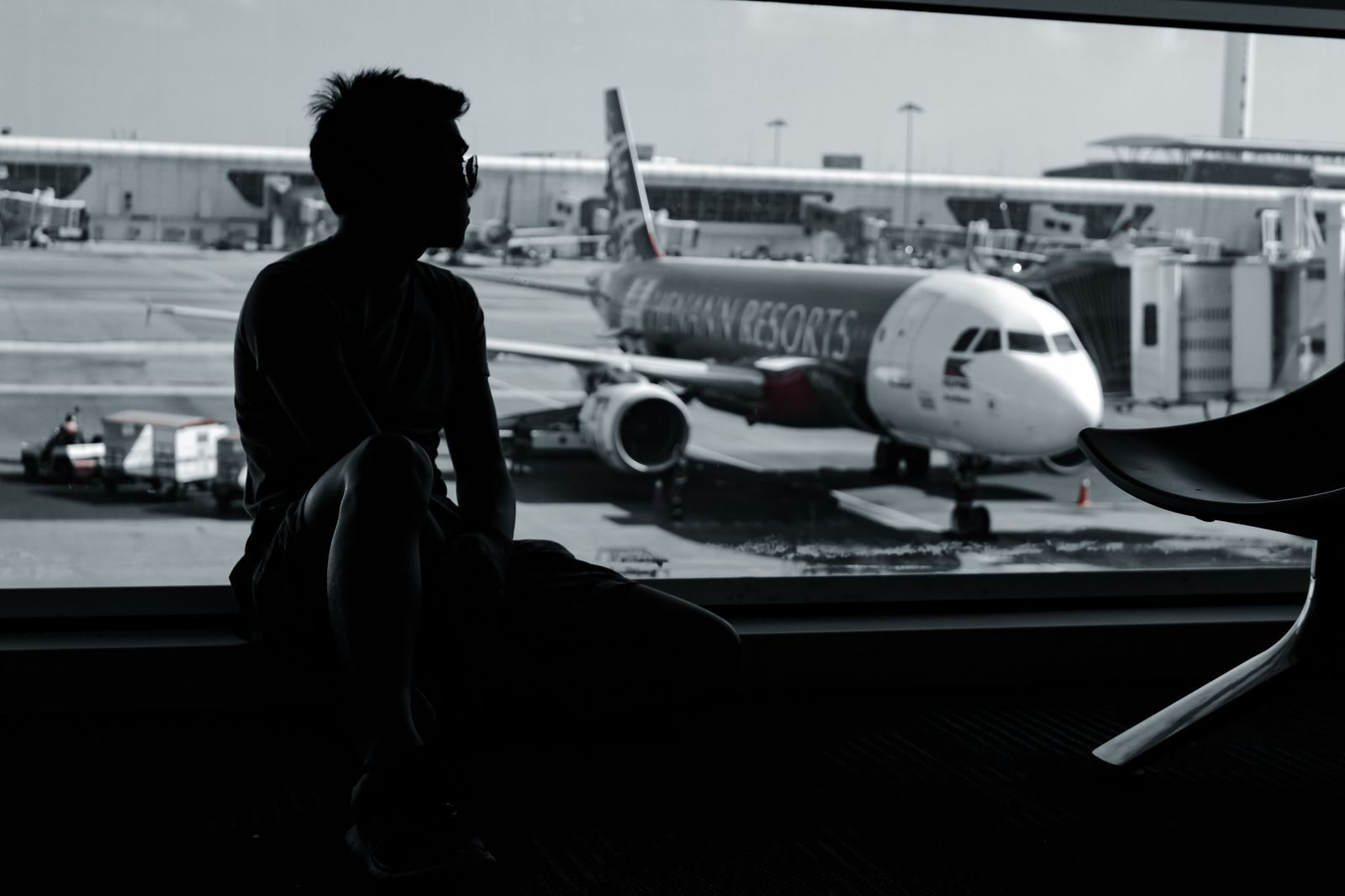 A traveller wheeling a suitcase through a bright airport terminal towards the exit
