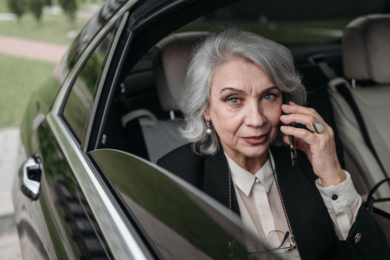 An executive speaking on the phone in the back seat of a black car with the window closed