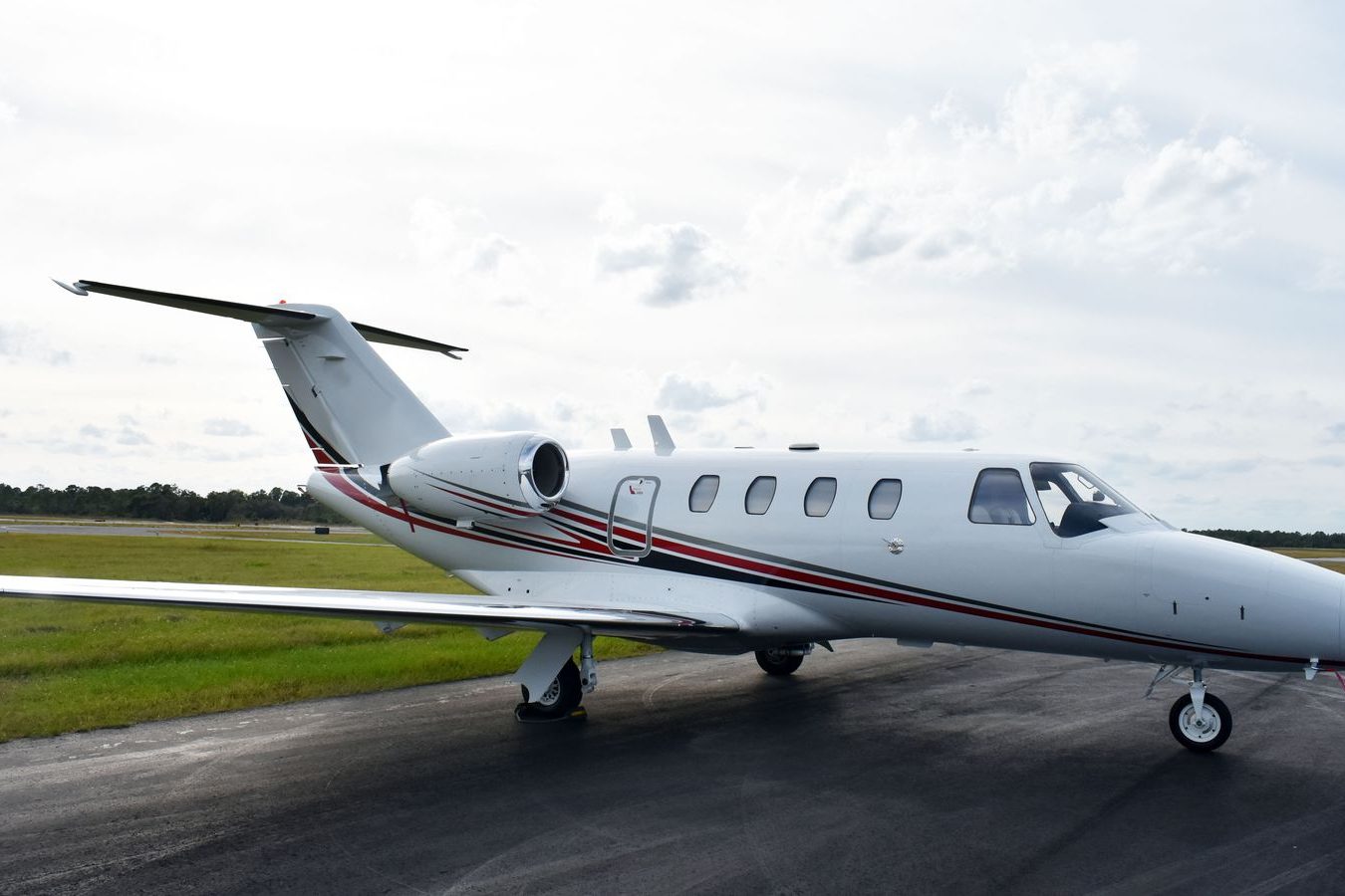 A black SUV parked beside a private jet on an apron with the chauffeur at the rear door