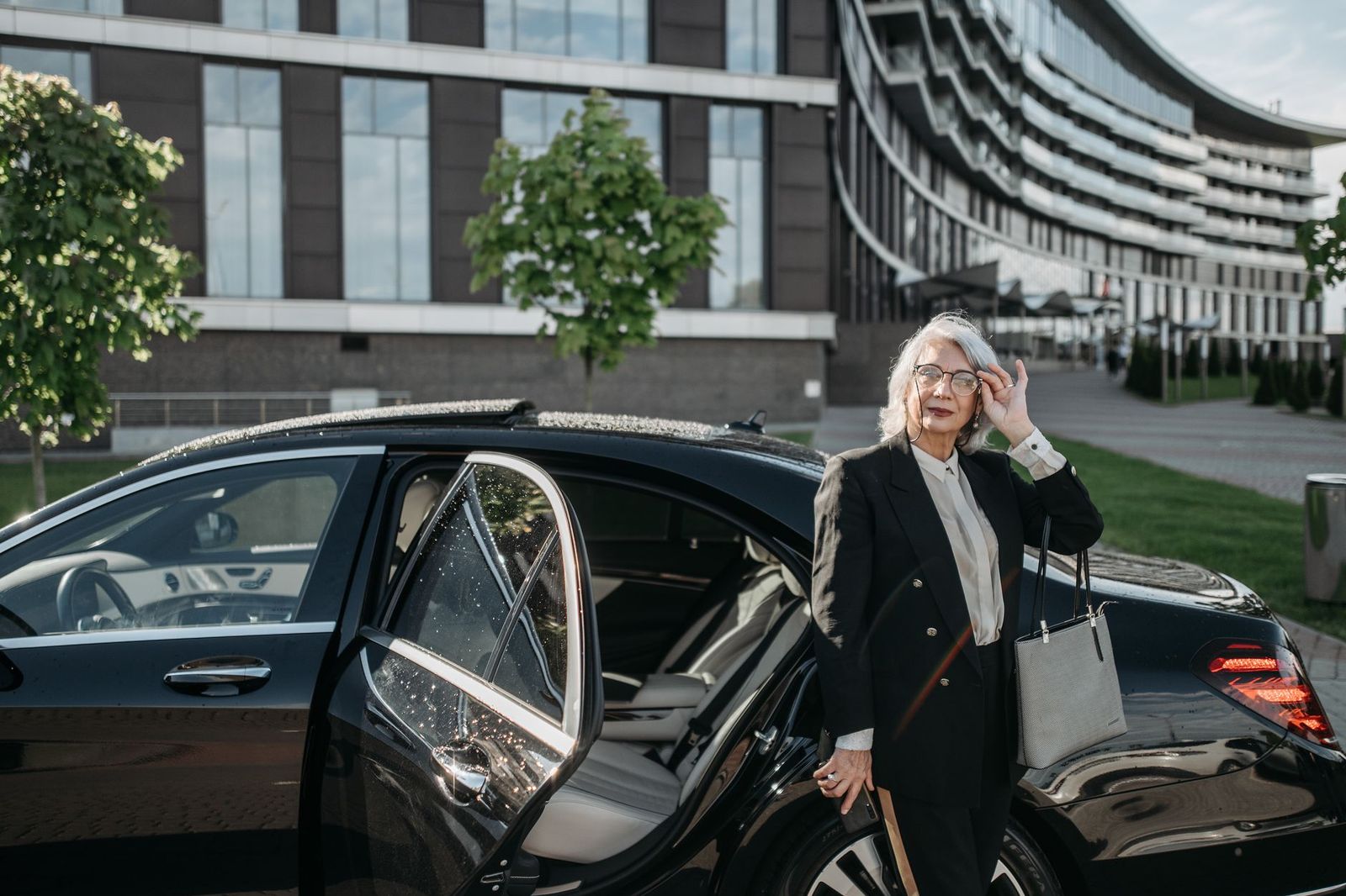 A chauffeur at the kerb outside an office tower: the waiting car is part of an hourly booking
