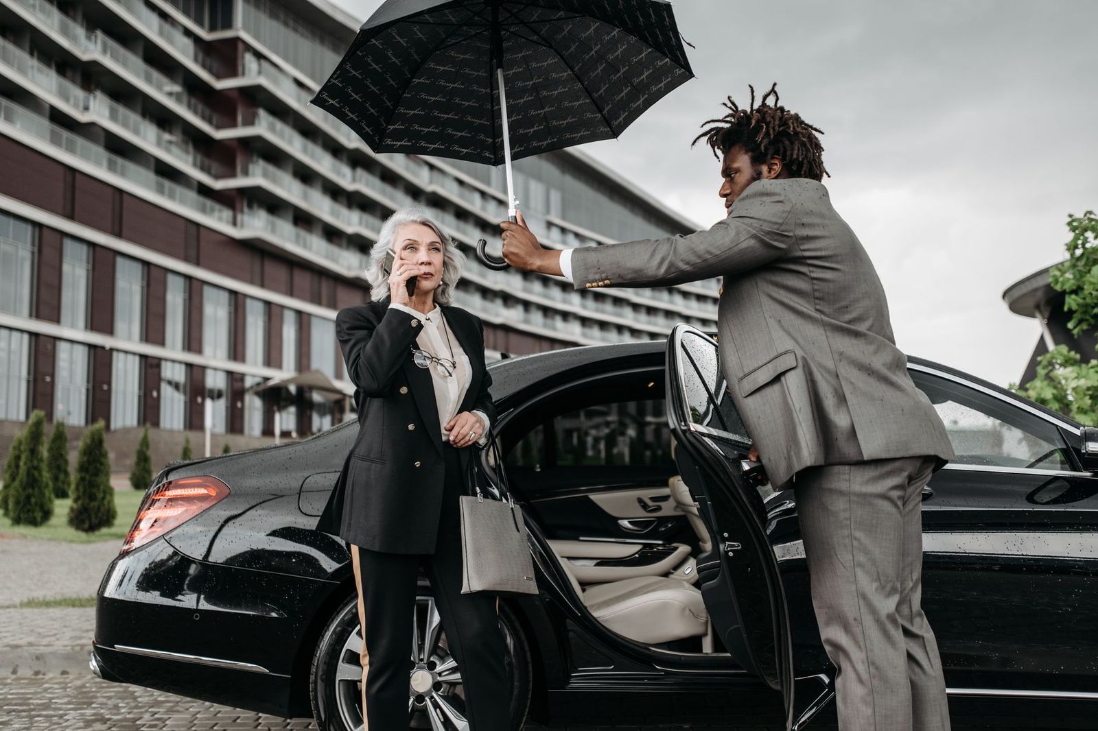A black SUV waiting at an airport arrivals curb with a chauffeur holding the door