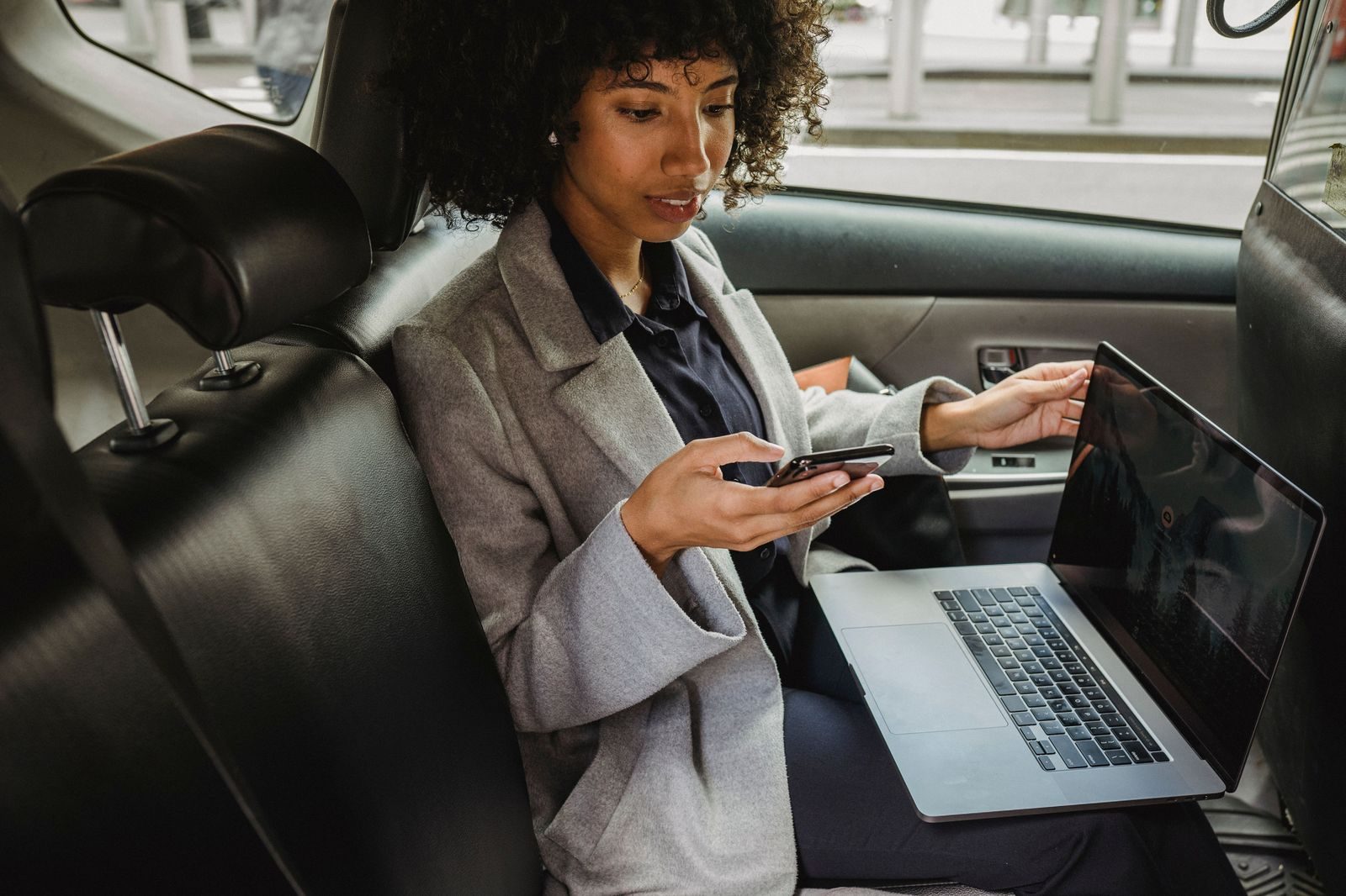 Passenger working on a laptop in the back seat of a black car on the highway