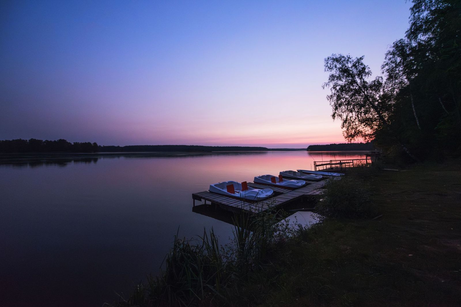 Muskoka chairs on a dock at sunset beside a calm lake